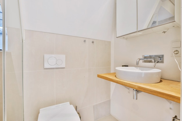 Lavabo de encimera moderno con grifo de pared debajo del armario con espejo en el baño con azulejos claros