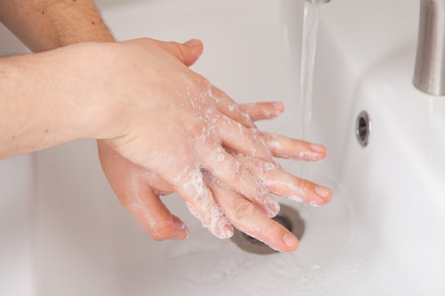 Lavado a mano con jabón closeup sobre el lavabo en el baño. Enjabonar las manos entre los dedos. Completamente desinfectado.