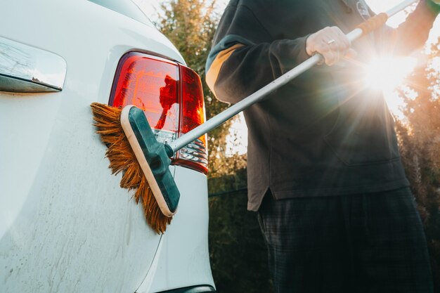 El lavado manual de automóviles el hombre lava el automóvil con un cepillo de escoba afuera en el territorio de una casa privada