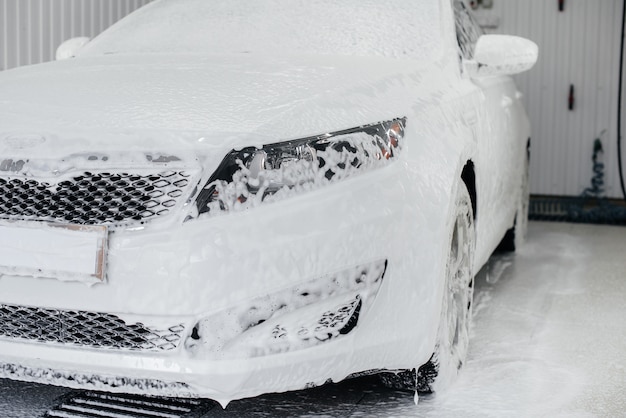 Lavado moderno con espuma y agua a alta presión de un automóvil blanco. Lavado de autos.