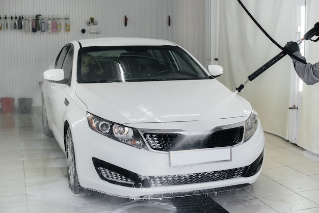 Lavado moderno con espuma y agua a alta presión de un automóvil blanco. Lavado de autos.