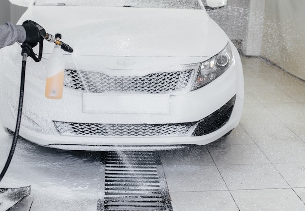 Lavado moderno con espuma y agua a alta presión de un coche blanco. Lavado de autos.