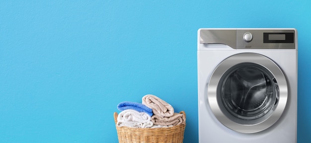Lavadora con ropa cerca de toallas de baño limpias en canasta de mimbre sobre fondo de pared azul