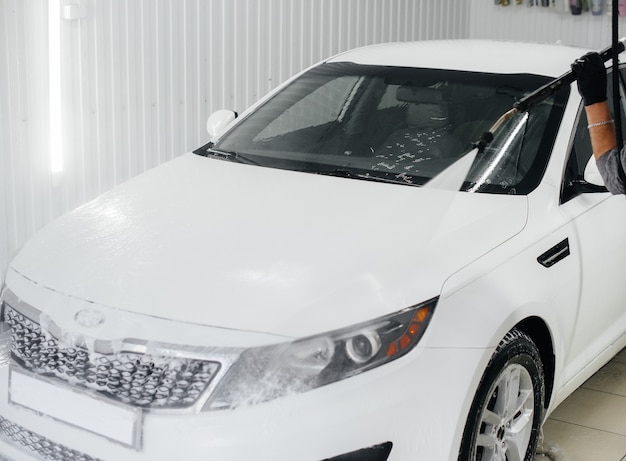 Foto lavagem moderna com espuma e água a alta pressão de um carro branco. lava-jato.