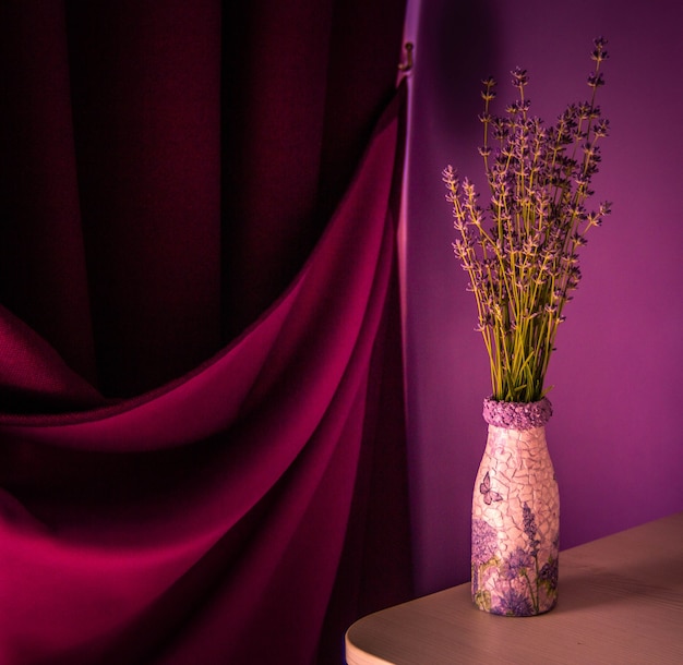 Lavanda no vaso sobre a mesa. Cortina roxa e fundo de parede violeta.