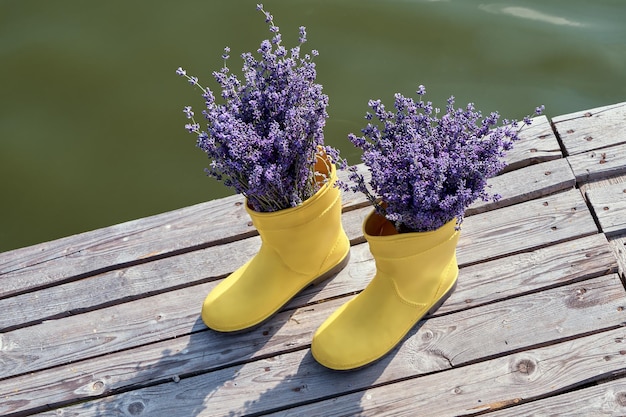 Lavanda roxa em botas de borracha amarela em um cais perto de um rio