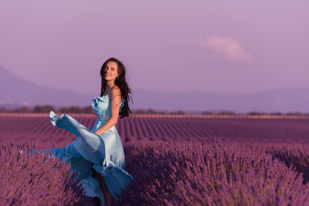 Lavander Blumenfeld Frau in cyanfarbenem Kleid, die Spaß hat und sich im Wind im lila Blumenfeld entspannen kann