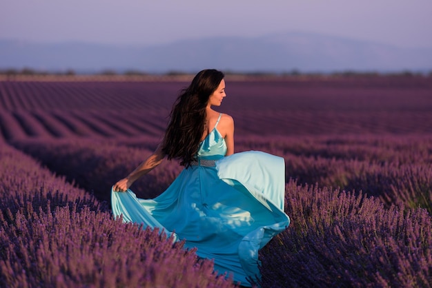 Lavander Blumenfeld Frau in cyanfarbenem Kleid, die Spaß hat und sich im Wind im lila Blumenfeld entspannen kann