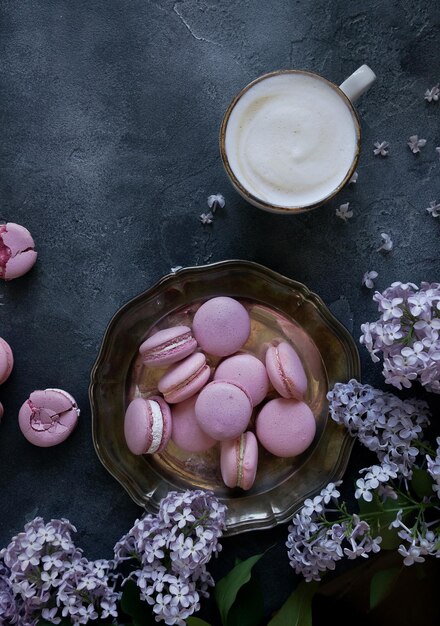 Lavander- und Heidelbeer-Macarons und Cappuccino-Kaffee auf dunklem Steintisch mit lila Blüten