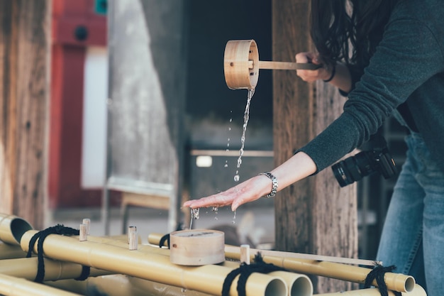 Lavando as mãos no pavilhão de água no templo japonês osaka japão. experiência de viagem fotógrafa feminina ásia purificação de cultura de religião tradicional usando vara de madeira de bambu como ferramenta em shitennoji.