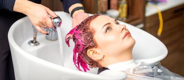 Lavando o cabelo feminino tingido Uma jovem mulher caucasiana tendo o cabelo lavado em um salão de beleza Cabeleireiro profissional lava a tinta de cor rosa do cabelo de um cliente