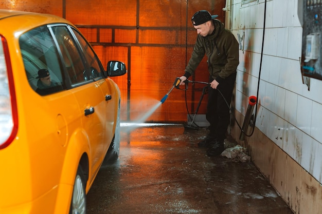 Lavando um carro amarelo em uma lavagem de carros self-service sem contato Lavando um carro sedan com espuma e água de alta pressão