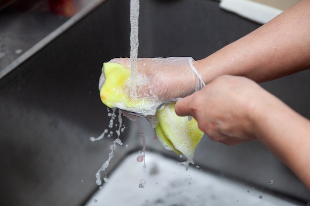 Lavarse las manos con espuma y una esponja bajo el agua del grifo.