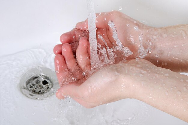 Lavarse las manos bajo el grifo de agua sin jabón Detalle del concepto de higiene Mano humana y chorro de agua