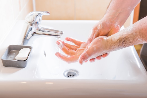 Lavarse las manos hombre enjuagar el jabón con agua corriente en el fregadero, prevención de coronavirus higiene de las manos.