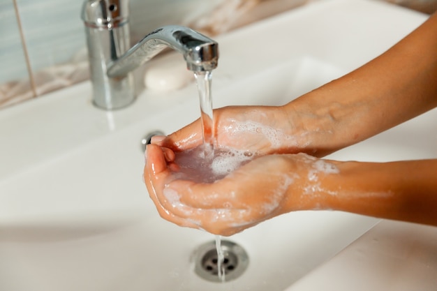 Lavarse las manos con jabón con agua corriente del grifo. manos femeninas bajo el chorro de agua.