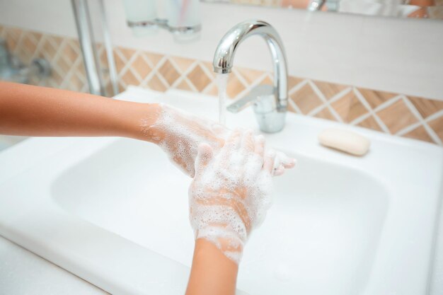 Lavarse las manos con jabón bajo el grifo con agua El niño se lava las manos El concepto de higiene Enfoque selectivo