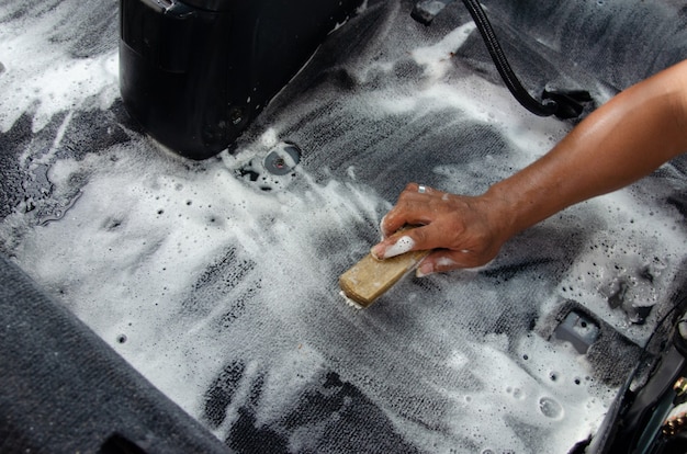 Lave la alfombra del automóvil. Detallando el interior de un automóvil moderno. Limpie con un cepillo y una solución de limpieza en la alfombra del automóvil.