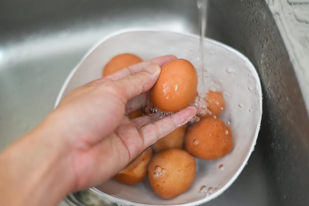 Lave los huevos, lave los huevos a mano en el tazón en el fregadero, limpie los huevos de gallina frescos