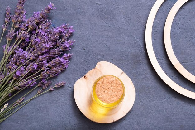 Lavendelblüten und Flasche mit gelbem Öl auf Holzpodest auf dunklem Hintergrund Wellness Flat Lay Konzept