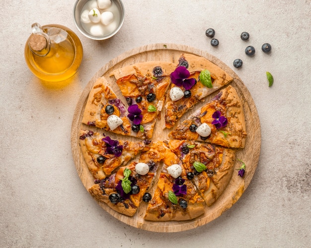 Foto lay flat de deliciosa rebanada de pizza con arándanos y pétalos de flores