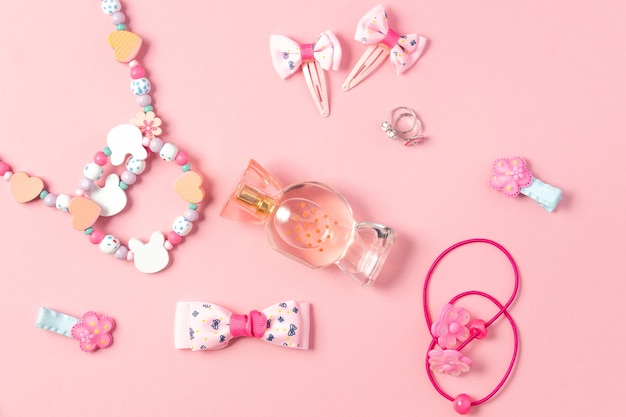 Foto lay flat para niños. perfume en forma de caramelos, bisutería infantil y complementos para el cabello sobre un fondo rosa. accesorios para niñas.