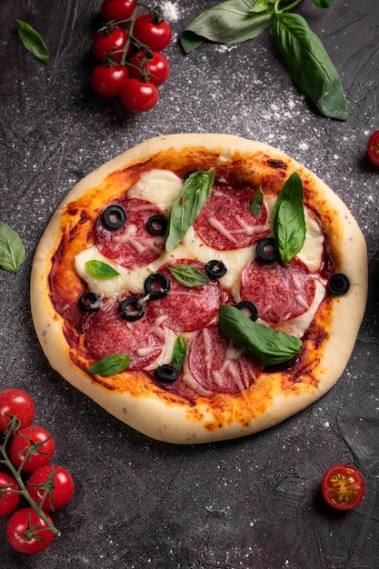 Lay Flat de pizza recién horneada con aceitunas y albahaca e ingredientes sobre un fondo negro