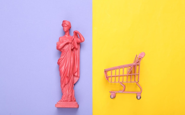 Layout criativo Estátua de deusa grega antiga rosa com carrinho shupermarket em fundo amarelo roxo Vista superior plana