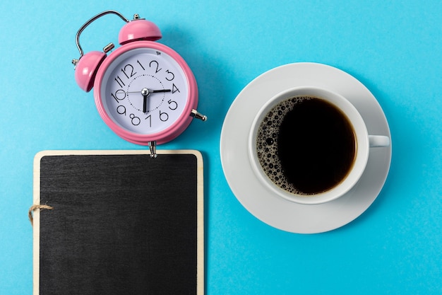 Foto layout criativo feito com uma xícara de café e despertador sobre fundo azul.