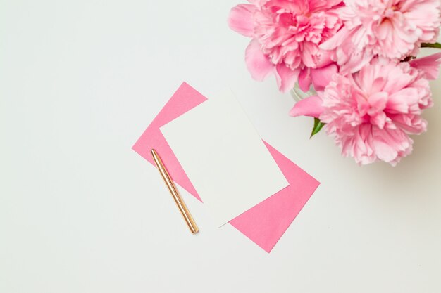 Layout criativo feito de envelope de papel rosa com uma caneta de ouro, um buquê de peônias rosa isolado no branco