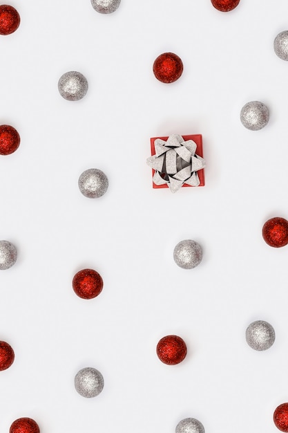 Layout de feriado brilhante com bolas vermelhas e prateadas cintilantes e uma pequena caixa para presente com laços de ouropel