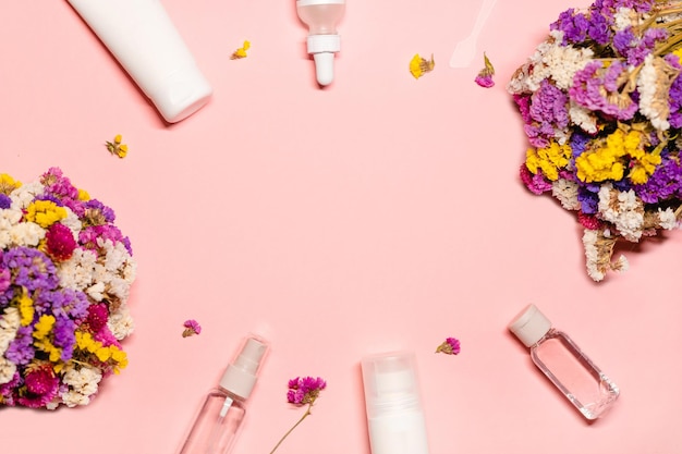 Foto layout fotografado com produtos de beleza e flores ao redor do espaço de cópia em um fundo rosa pastel