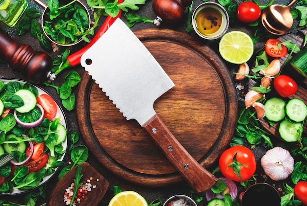 Layout für gesunde vegane Zutaten Flatlay aus grünen Kräutern, Tomaten, Gurken, Gewürzen und Öl auf braunem Küchentisch mit Holzbrett und Beilmesser Draufsicht Vegetarisches Konzept für sauberes Essen