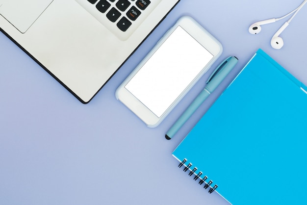 Layout mit einem Laptop, Telefon, Notizblock und Kopfhörern auf einem blauen Hintergrund. Platz für Text. Layout der Flat Lay Desktop Tools