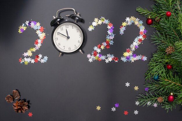 Layout sobre o tema do ano novo 2022 com números, relógios, brinquedos e galhos de uma árvore de natal em um fundo escuro.