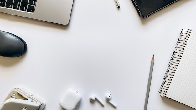 Foto layout sobre o tema do processo de trabalho ou educação em um fundo branco com bloco de notas, caneta, laptop, mouse de computador, tablet, furador, fones de ouvido, lápis. camada plana, vista superior.