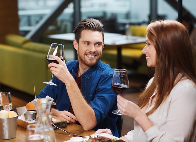 lazer, alimentação, comida e bebida, conceito de pessoas e feriados - casal sorridente jantando e bebendo vinho tinto no restaurante