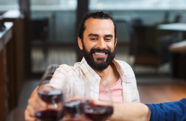 Foto lazer, alimentação, comida e bebida, conceito de pessoas e feriados - homem feliz com amigos tilintando copos de vinho no restaurante