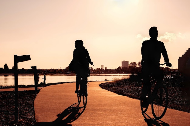 Lazer ativo na cidade ao pôr do sol silhuetas de uma mulher e um homem de bicicleta