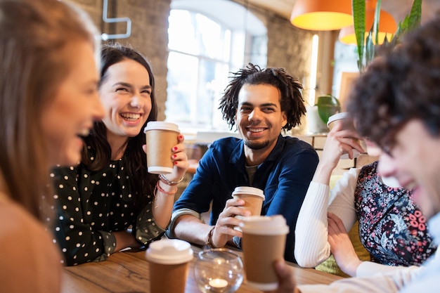 lazer, bebidas, pessoas e conceito de comunicação - amigos felizes bebendo café em copos de papel descartáveis no restaurante ou café