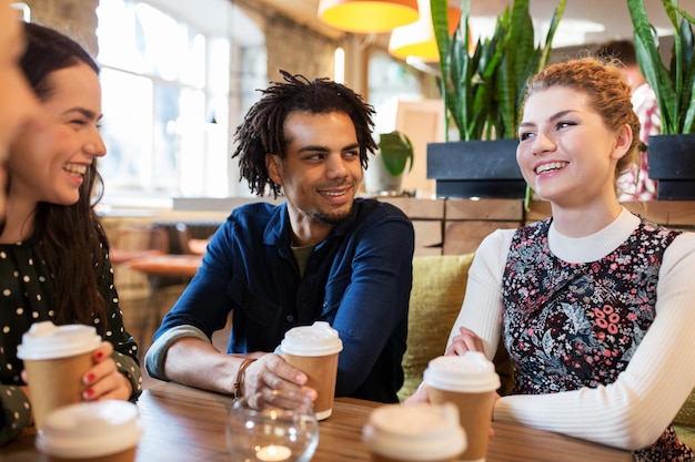 lazer, bebidas, pessoas e conceito de comunicação - amigos felizes bebendo café em copos de papel descartáveis no restaurante ou café