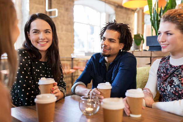 lazer, bebidas, pessoas e conceito de comunicação - amigos felizes bebendo café em copos de papel descartáveis no restaurante ou café