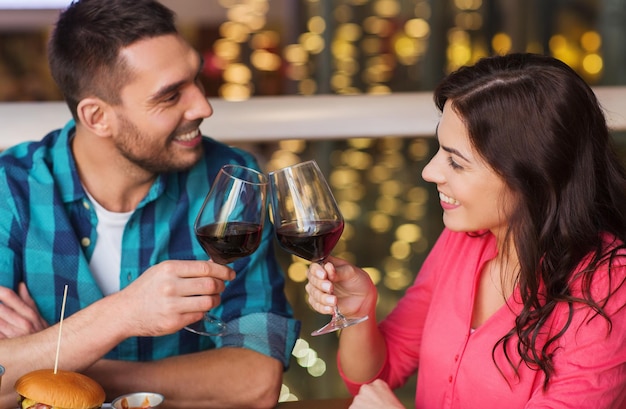 Foto lazer, celebração, comida e bebida, conceito de pessoas e feriados - casal sorridente jantando e bebendo vinho tinto no restaurante