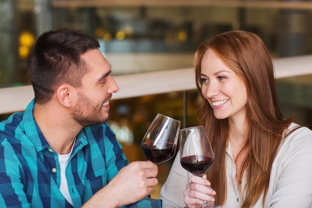 lazer, celebração, comida e bebida, conceito de pessoas e feriados - casal sorridente jantando e bebendo vinho tinto no restaurante