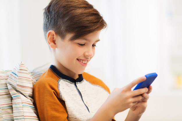 lazer, crianças, tecnologia, comunicação na internet e conceito de pessoas - menino sorridente com mensagem de texto de smartphone ou jogo em casa