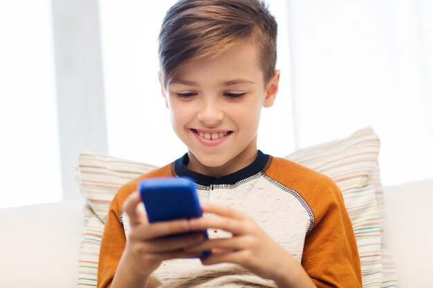 lazer, crianças, tecnologia, comunicação na internet e conceito de pessoas - menino sorridente com mensagem de texto de smartphone ou jogo em casa