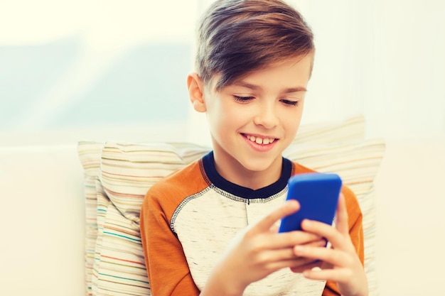 lazer, crianças, tecnologia, comunicação na internet e conceito de pessoas - menino sorridente com mensagem de texto de smartphone ou jogo em casa