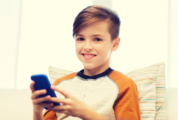 lazer, crianças, tecnologia, comunicação na internet e conceito de pessoas - menino sorridente com mensagem de texto de smartphone ou jogo em casa