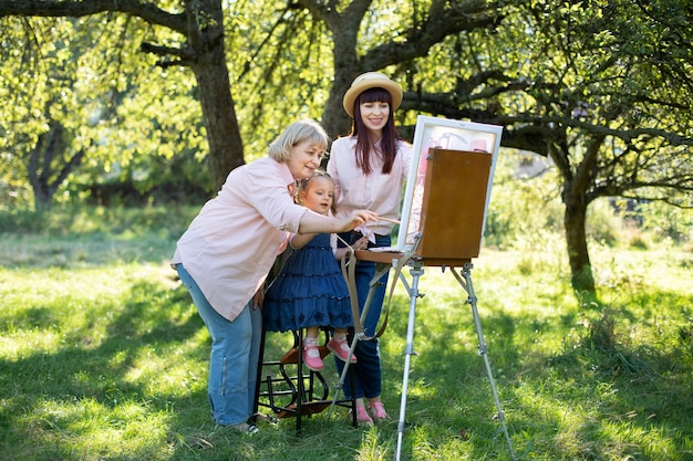 Lazer de verão em família com passatempo de pintura. Retrato ao ar livre de uma família de mulheres de três gerações, passando um tempo ao ar livre no parque, desenhando juntos na tela com tintas.