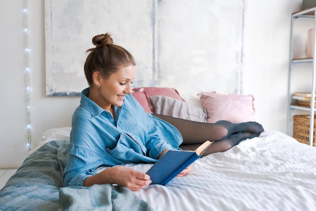 Lazer e conceito de pessoas jovem lendo livro na cama na camisa azul